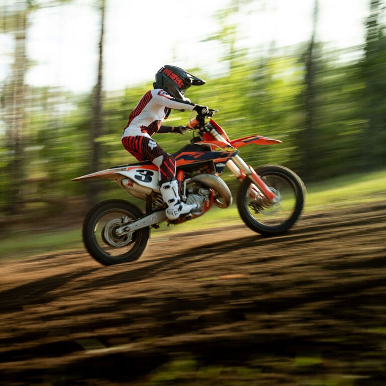 Young dirt biker riding a trail in the forest.