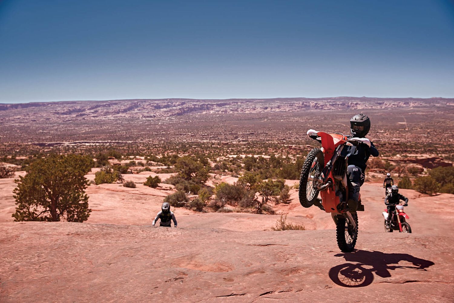 A dirt biking do a wheelie through a desert landscape. 